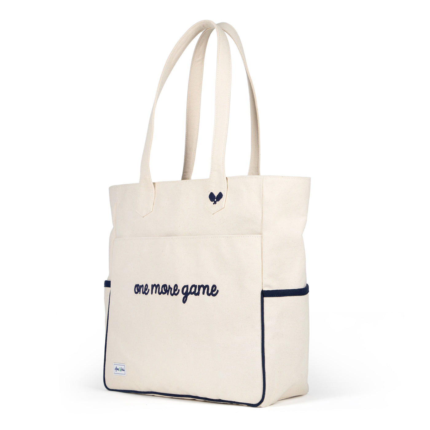 Tan canvas pickleball tote with slip pocket on front with a pickleball paddle inside. Front has navy embroidery that reads "one more game".