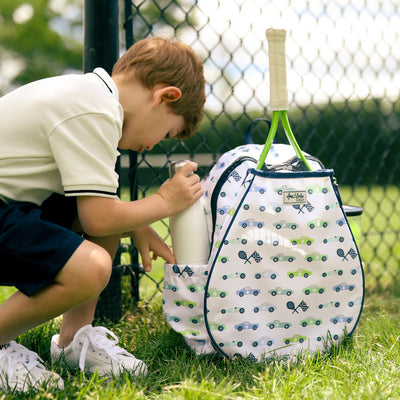 White kids tennis backpack with navy trim and blue and green racecars printed on the fabric. There is a tennis racquet in the front pocket.