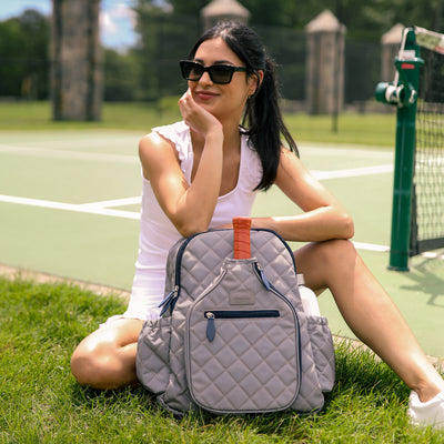 Quilted grey nylon with navy trim pickleball backpack with paddle shaped pocket on the front with paddle inside.