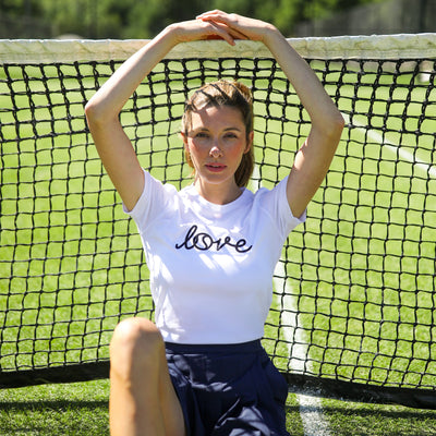 Woman sits on tennis court wearing white tshirt that says love